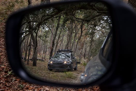 A rugged off-road vehicle captured in a car's side mirror, traversing a forested trail.