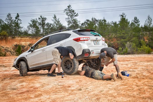 Three men work together to repair a vehicle in an outdoor setting, surrounded by trees and rocky terrain.