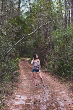 A woman in casual attire poses on a muddy forest path surrounded by dense trees.