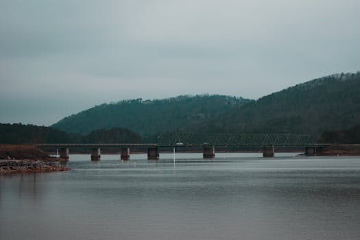 A tranquil view of a bridge crossing a calm body of water with mountains in the background.