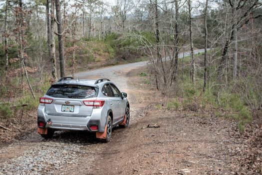 A silver SUV navigating a gravel road through a dense forest, showcasing off-road capabilities.
