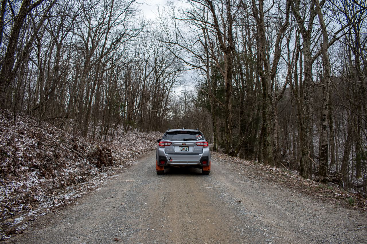 a car travels down a gravel road through a snow dusted forest in winte