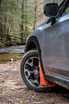 Close-up of an SUV wheel beside a scenic forest stream, perfect for nature exploration themes.