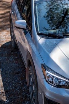 Close-up of a parked silver car on a gravel road with sunlight reflecting on the surface.