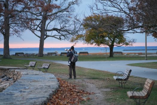 Photographer in a winter park taking pictures at sunset by the water.