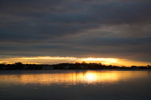Free Calm sunset reflecting on a peaceful lake beneath dramatic clouds. Stock Photo