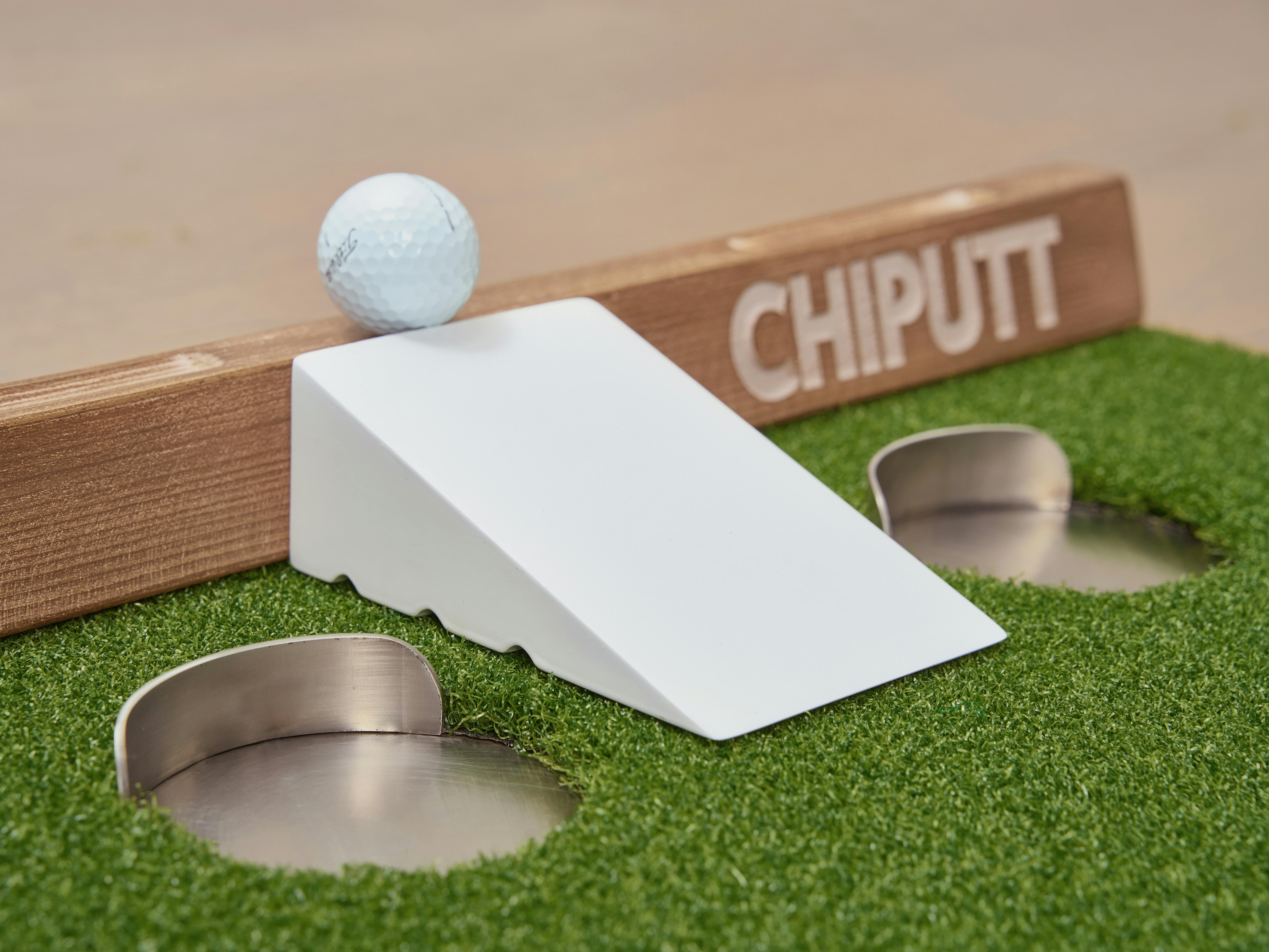 A golf ball on a white ramp with a 'CHIPUTT' board for practicing chipping and putting.