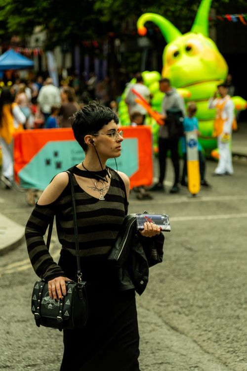 Free A stylish woman walks through a lively Dublin street event with colorful attractions in the background. Stock Photo
