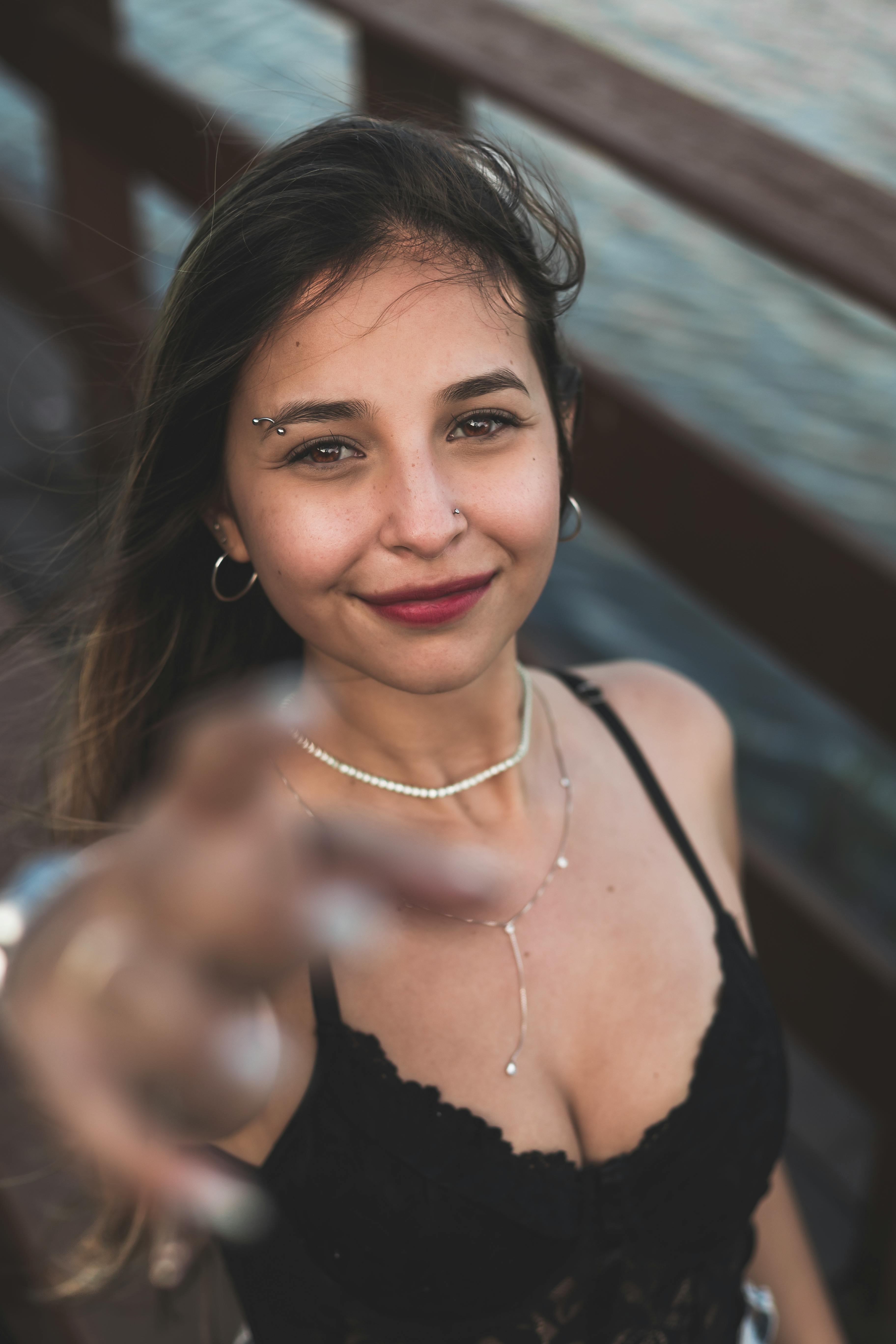 Gratis Ritratto di una giovane donna sorridente all'aperto, con gioielli e piercing, con una profondità di campo ridotta. Foto a disposizione