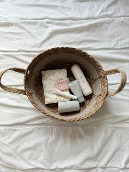 Woven basket with baby care products and cloth on a bed.