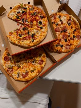 Three pizzas with various toppings in open cardboard boxes on a table.