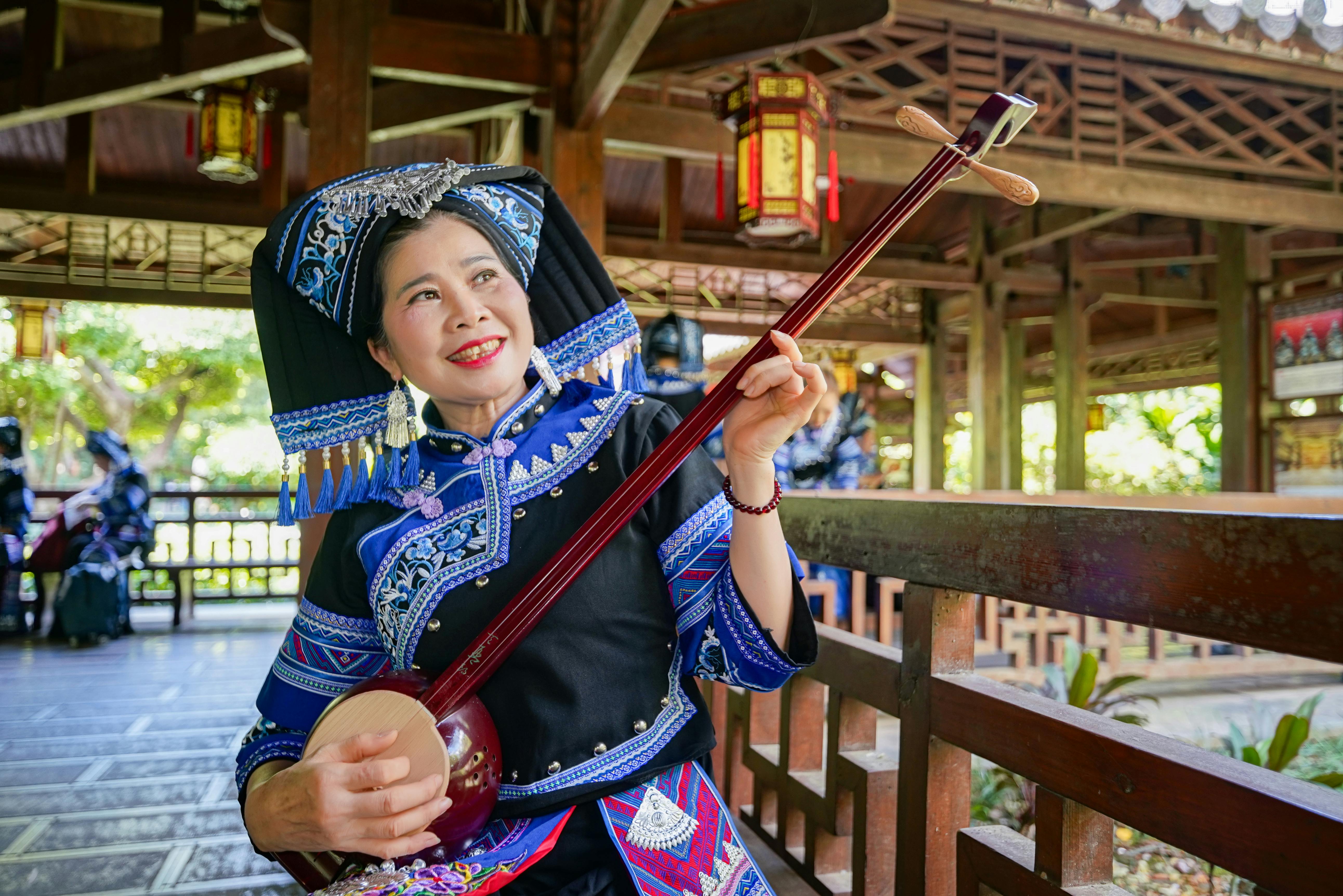 bezplatná Zhuangský hudebník v tradičním etnickém oděvu hrající venku na strunný nástroj. Základová fotografie