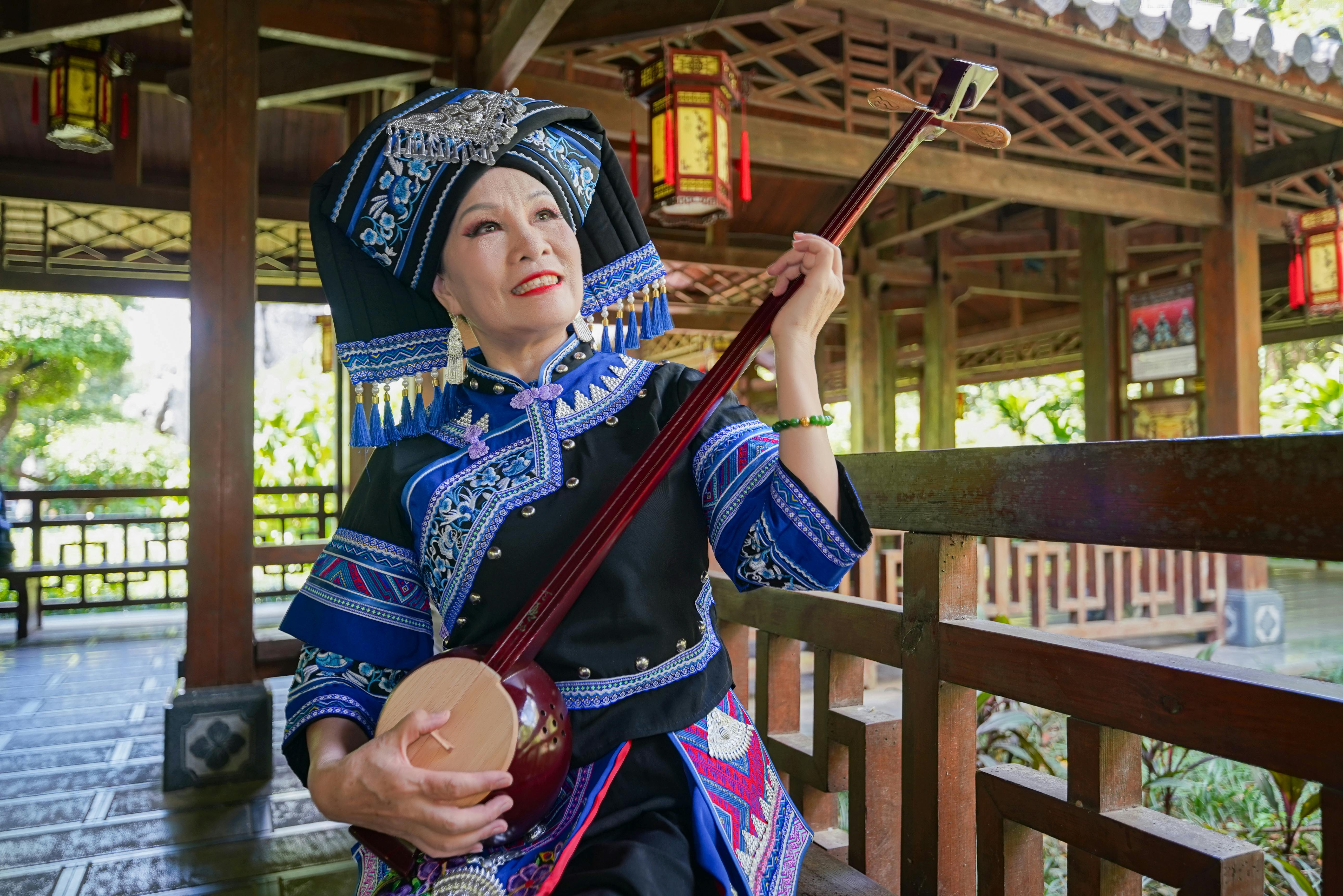 Безкоштовне Жінка Чжуан в етнічному одязі грає на традиційному китайському інструменті на вулиці. стокове фото