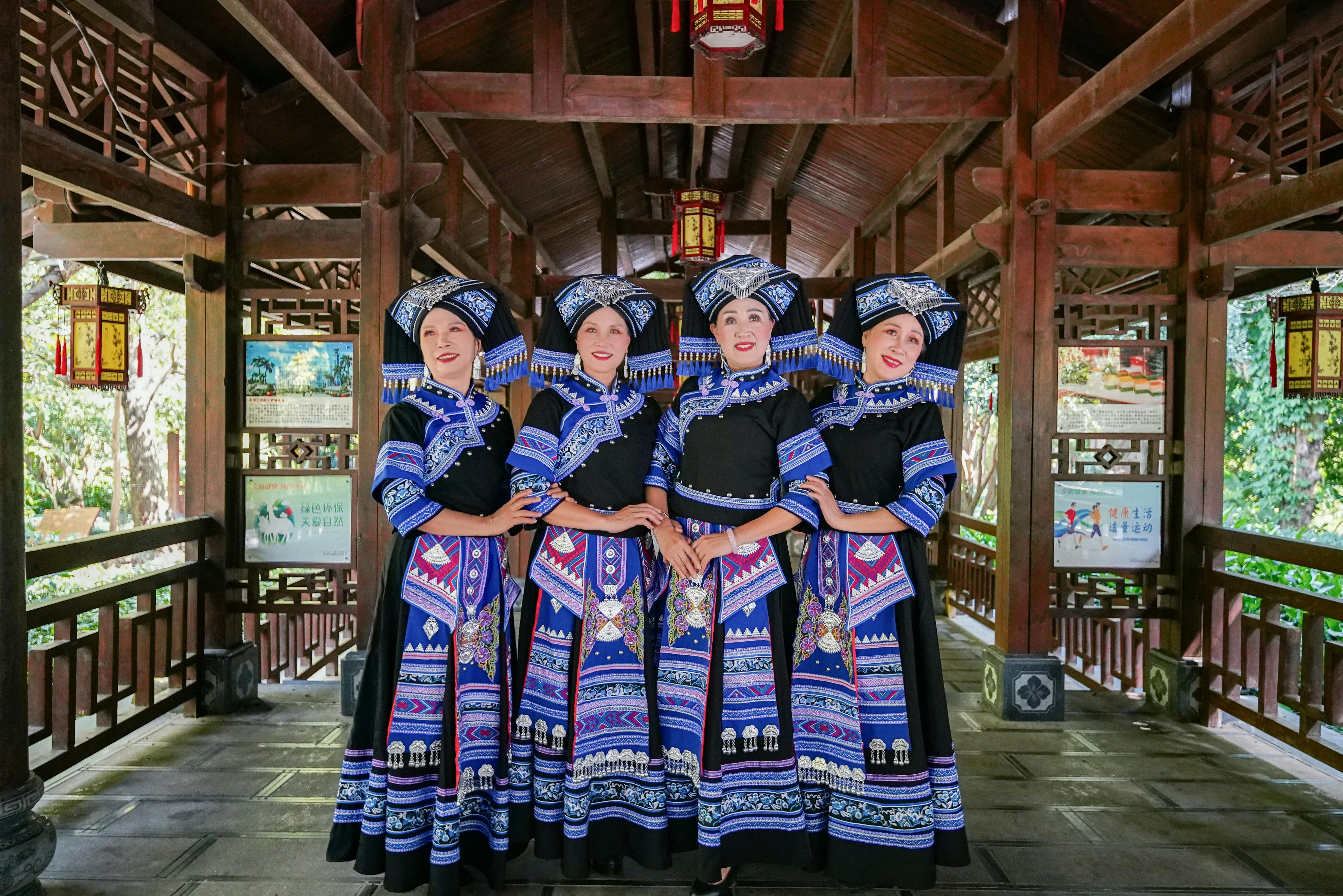 bezplatná Skupina žen v zářivých etnických krojích Čuang pózuje uvnitř v tradičním prostředí. Základová fotografie