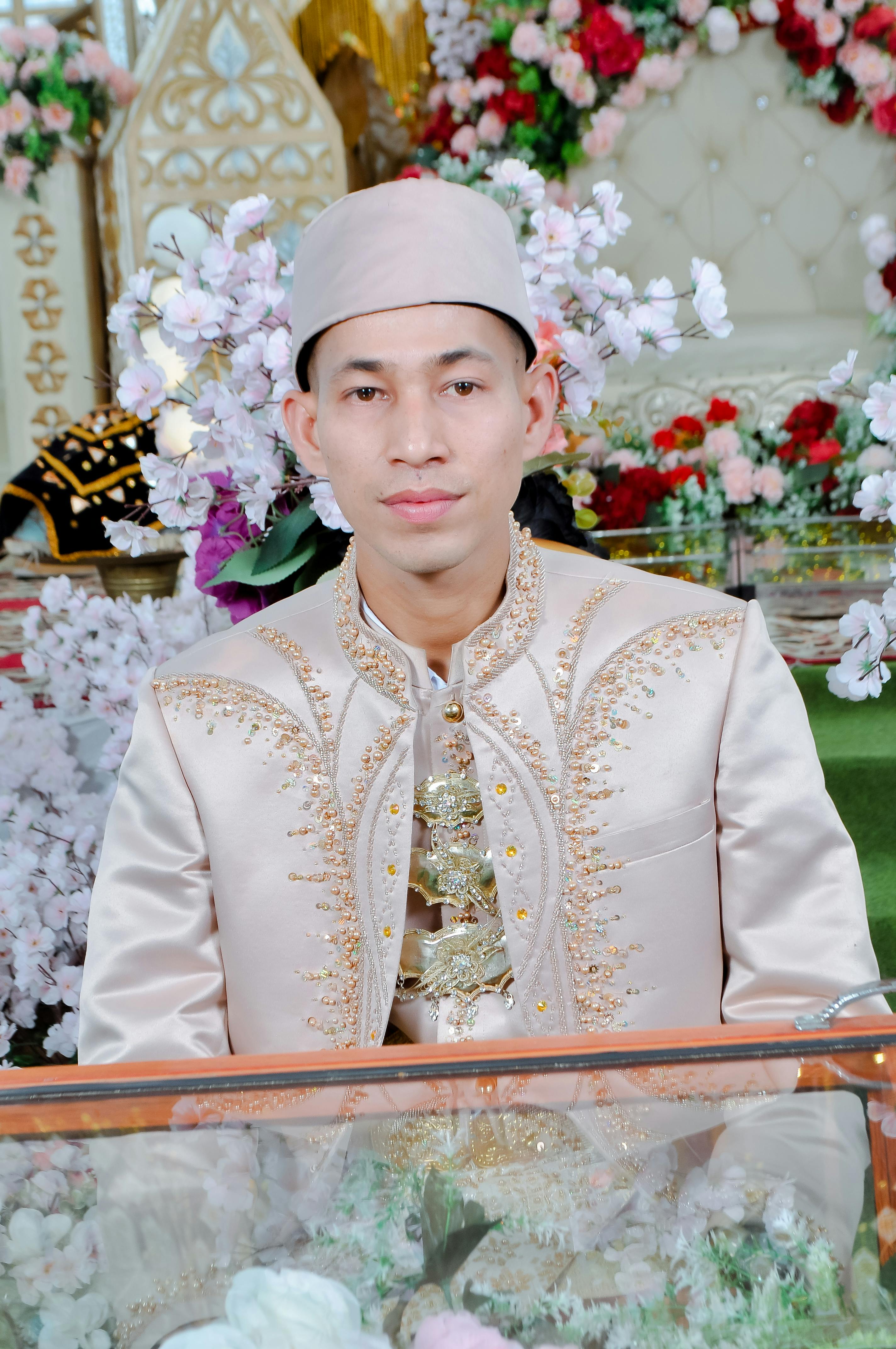 Man in traditional wedding attire posing indoors with floral decorations.