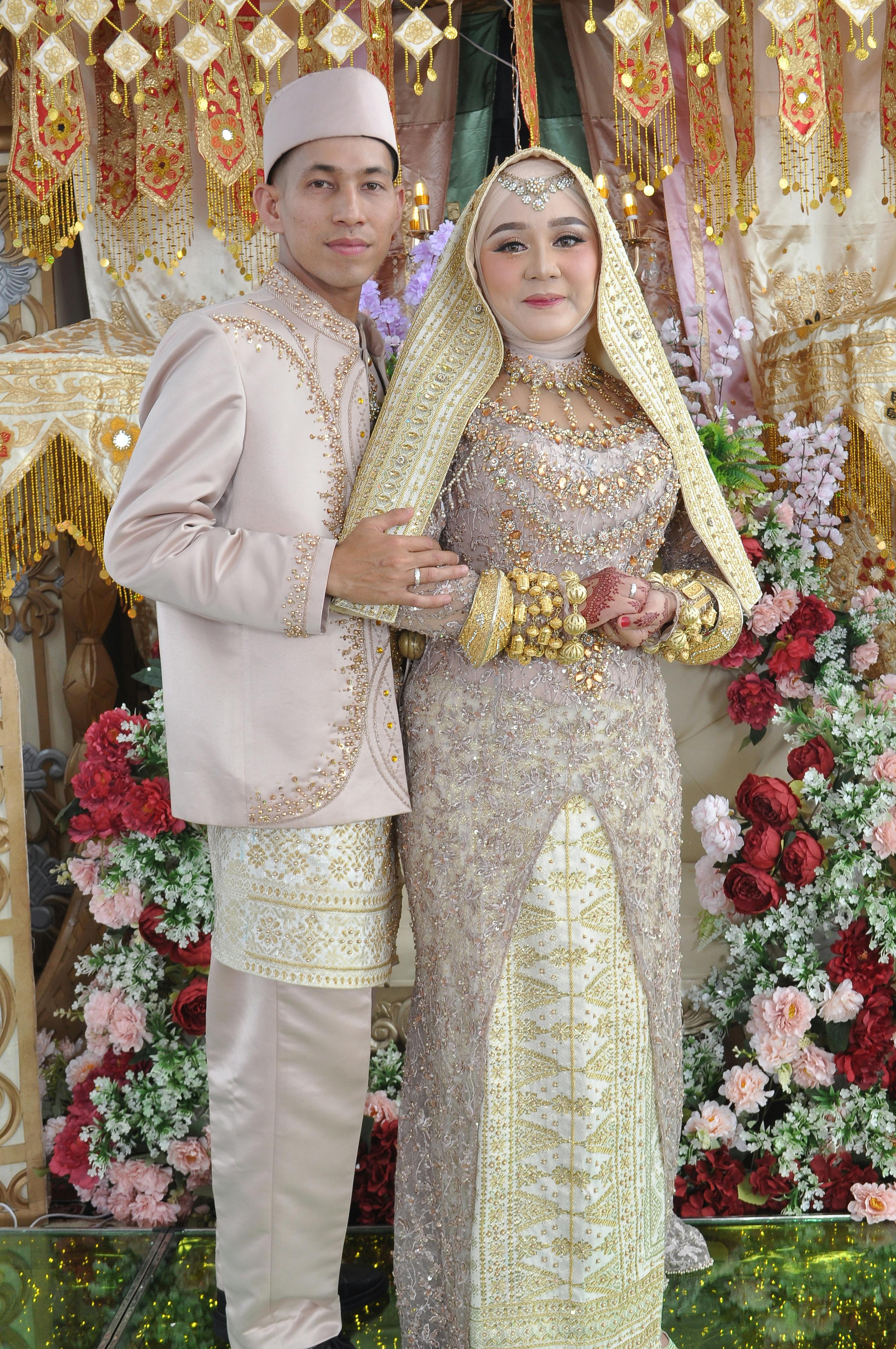 A couple in traditional wedding attire surrounded by floral decorations, celebrating cultural heritage.