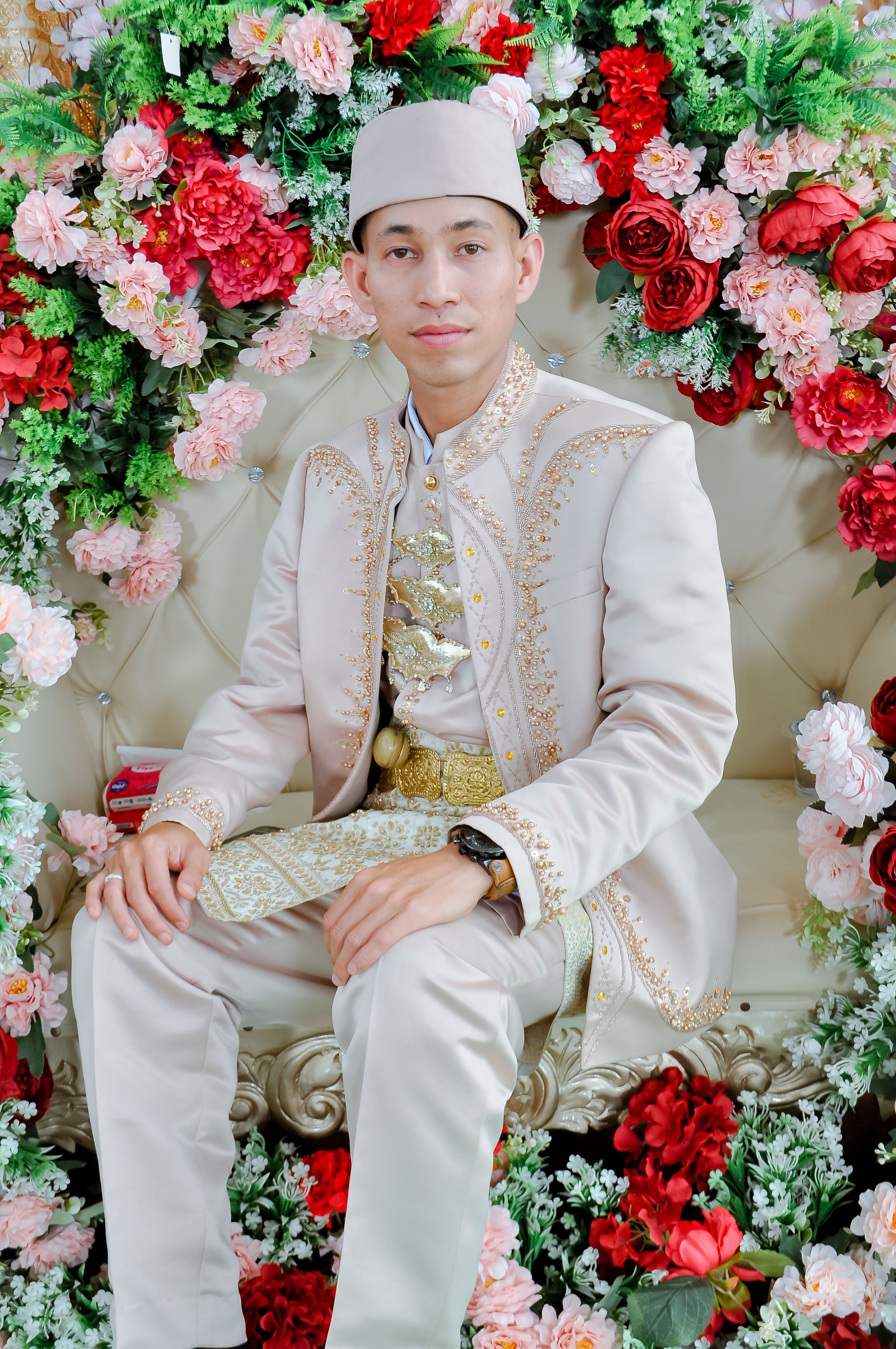 Man in traditional wedding attire surrounded by vibrant floral arrangement, exuding cultural elegance.