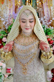 A bride wearing ornate traditional attire and intricate henna designs, surrounded by vibrant flowers.