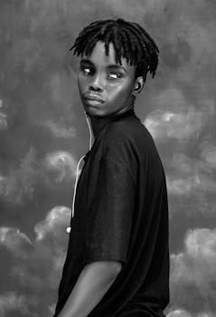 Artistic black and white portrait of a thoughtful teenager with dreadlocks looking off-camera.