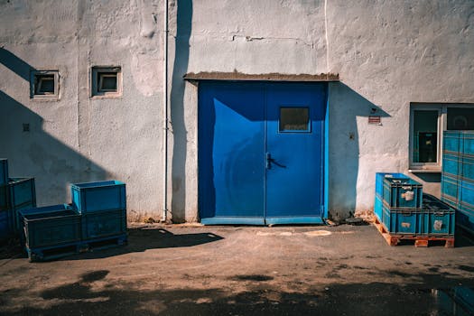 An industrial blue door surrounded by blue storage crates on a sunny day.