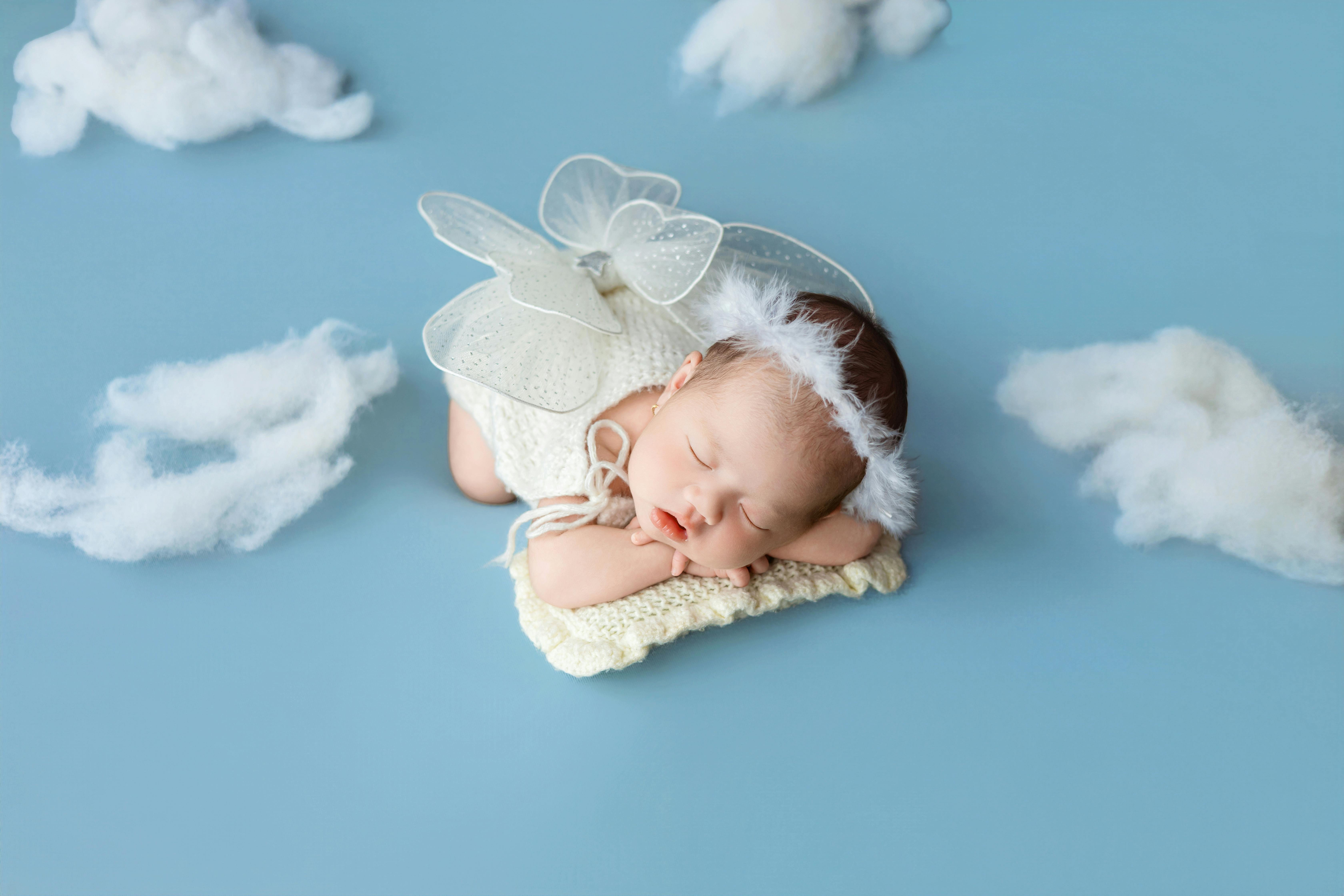 Cute newborn dressed as an angel sleeps on a cloud-like background in a studio setting.