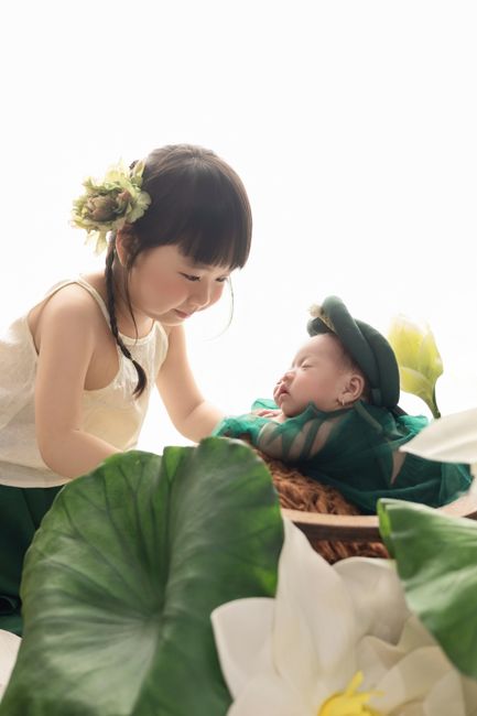 Adorable siblings in traditional dresses, surrounded by lotus leaves in a studio setting.