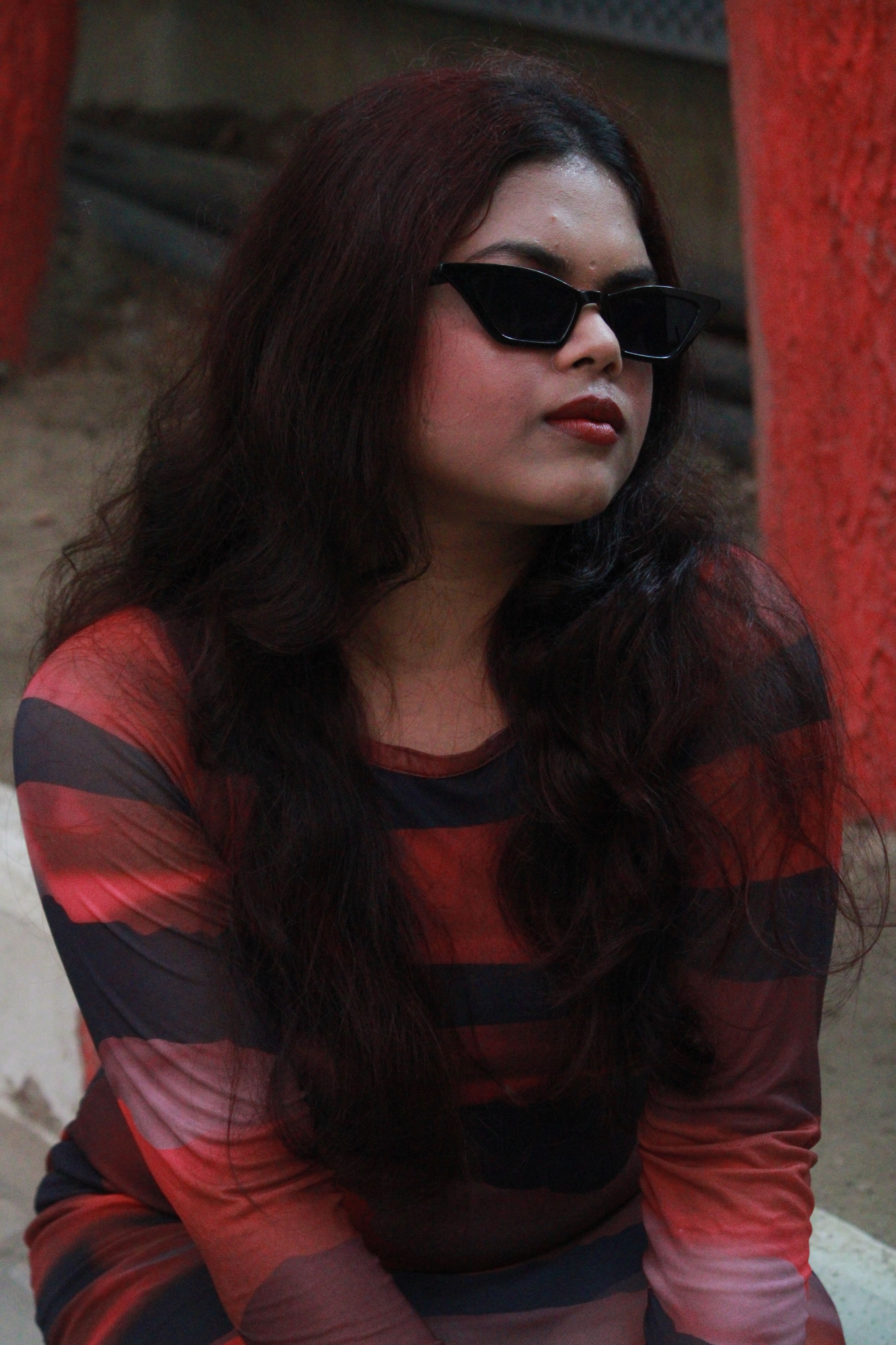 Portrait of a fashionable woman with long hair and sunglasses in an outdoor setting.
