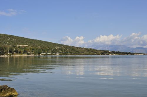 Free A tranquil coastal scene with reflective waters and distant mountains under a clear sky. Stock Photo
