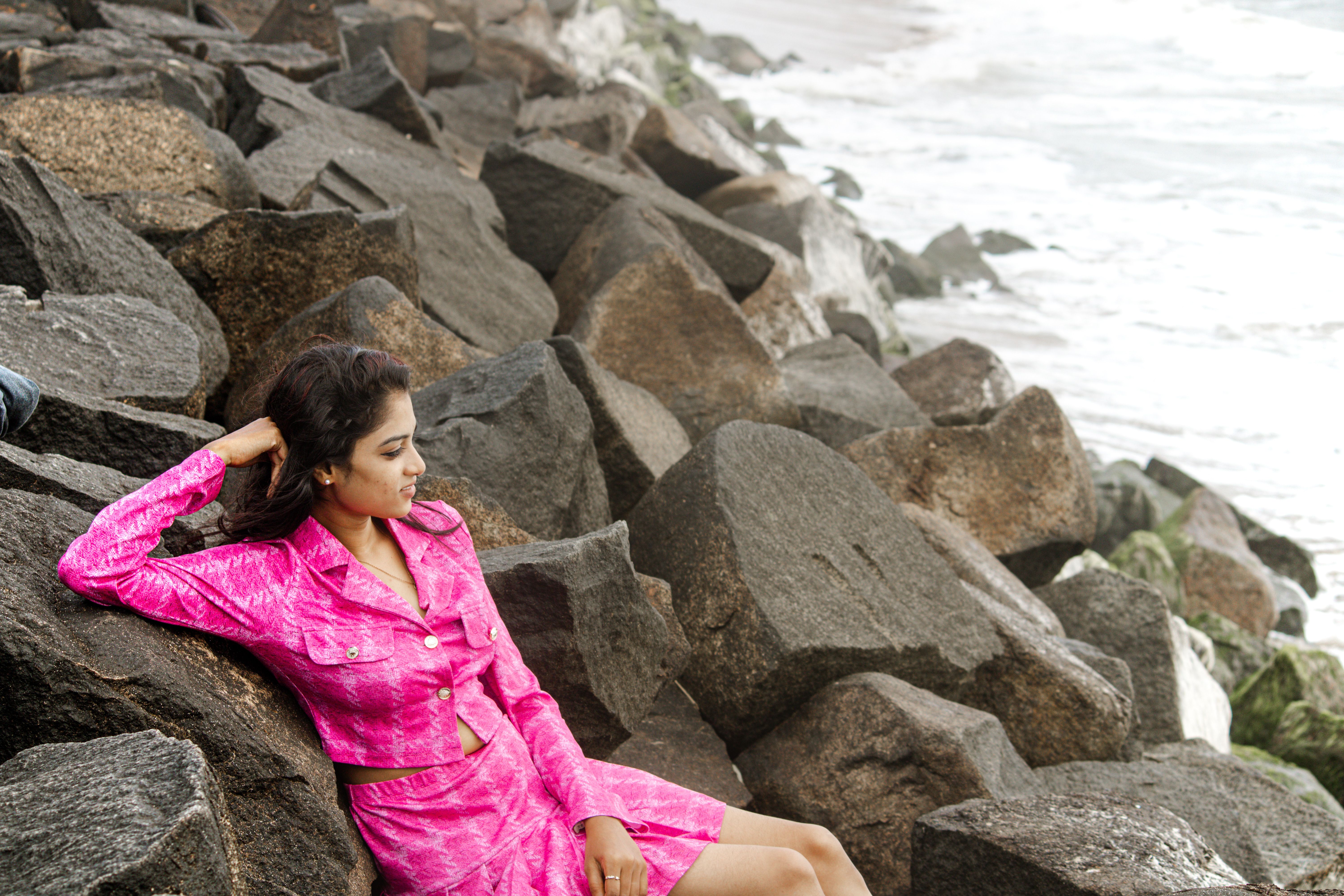 Young woman in vibrant pink outfit relaxing on rocky shoreline enjoying the view.