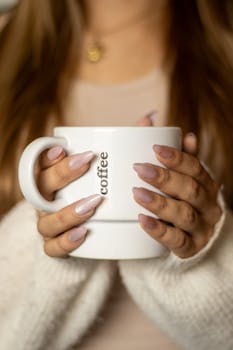 Cozy close-up of manicured hands holding a coffee mug with 'coffee' text.