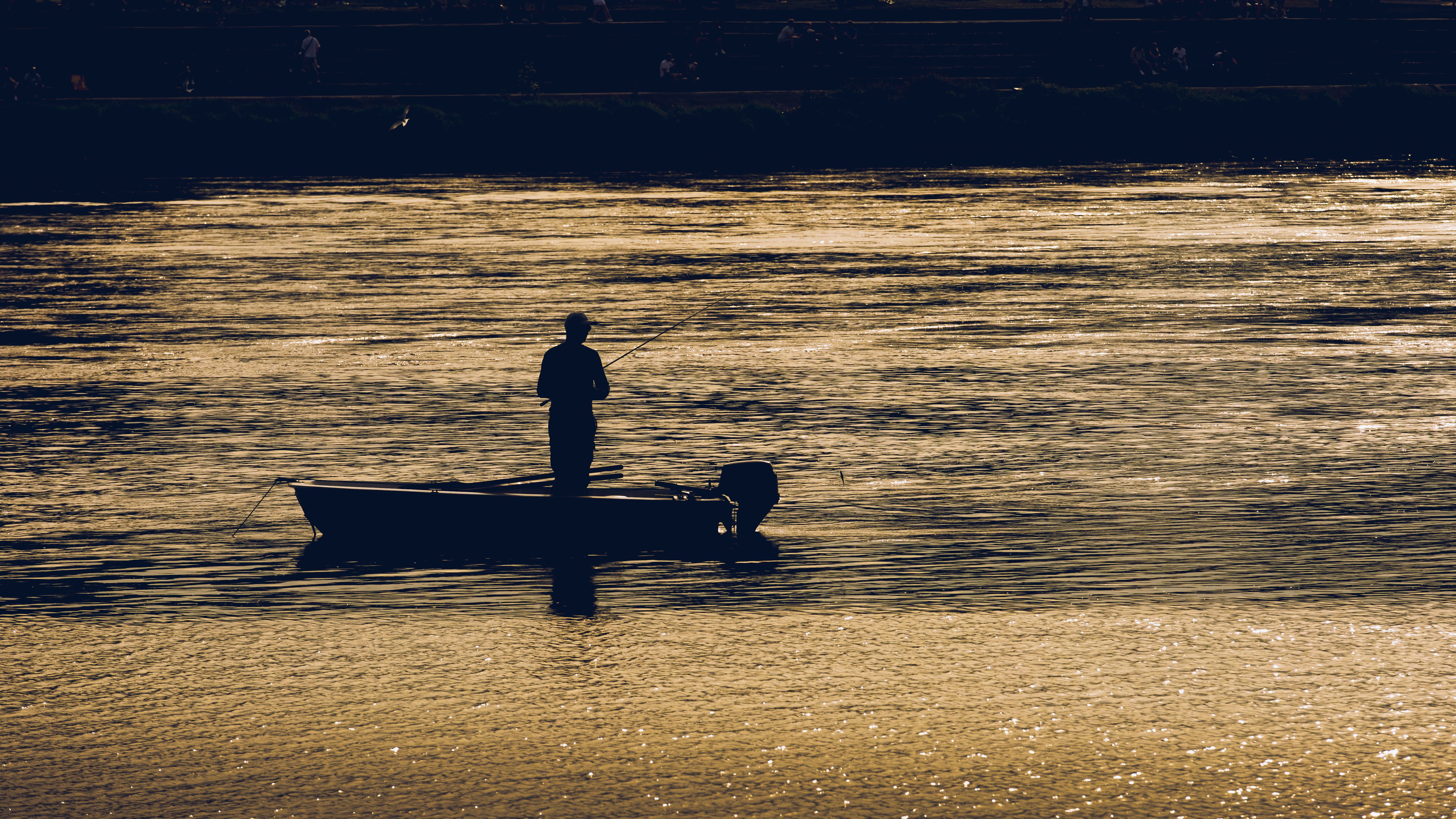 Silhouette of Fisherman on a Calm Lake at Sunset · Free Stock Photo