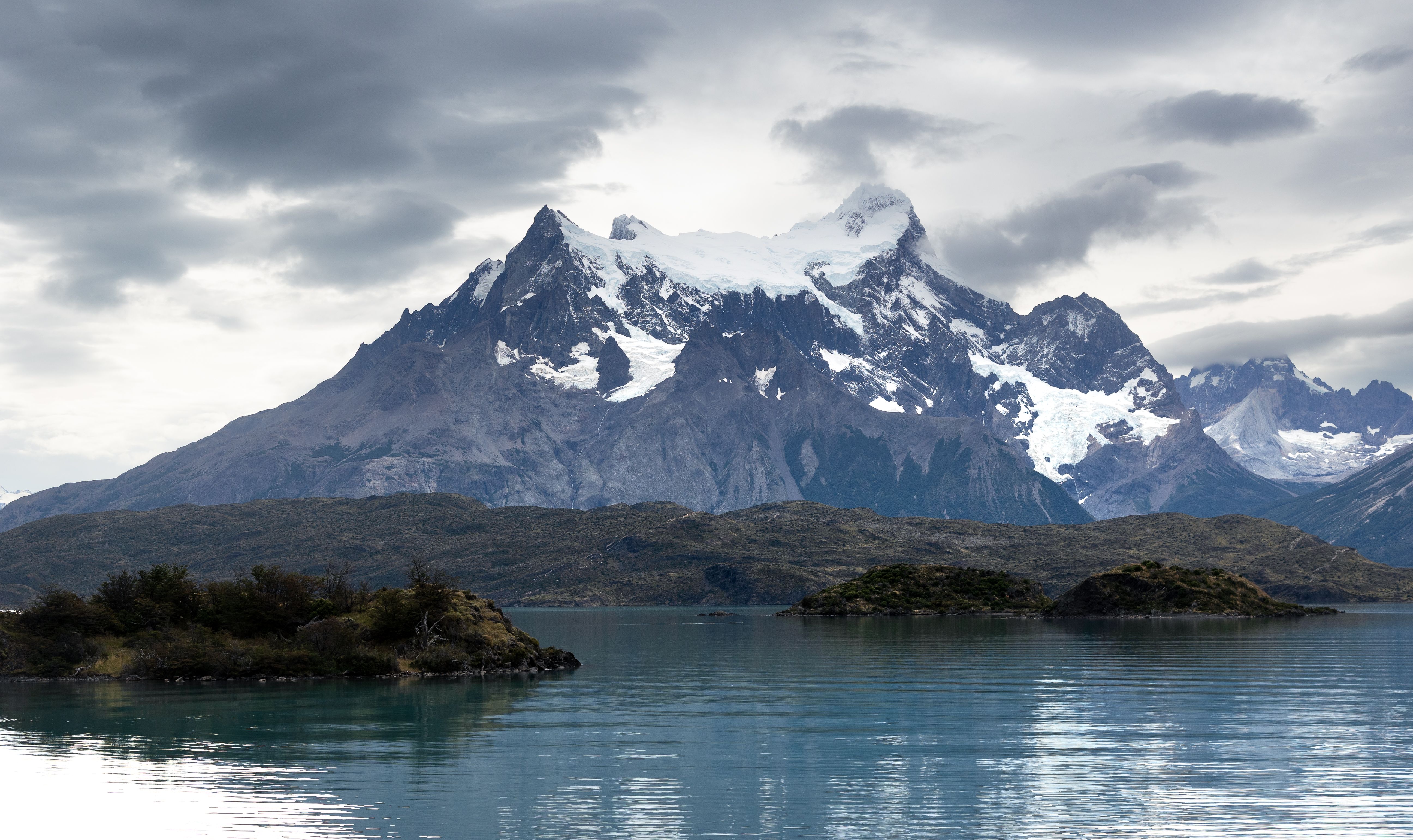 Dramatic landscape of Torres del Paine with snowy peaks and a serene lake under cloudy skies. Dramatic landscape of Torres del Paine with snowy peaks and a serene lake under cloudy skies.