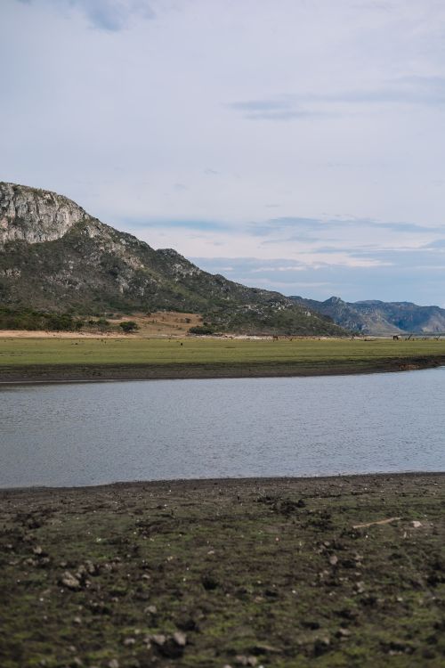 Free A tranquil mountain lake scene with rugged cliffs and clear blue skies, ideal for nature lovers. Stock Photo