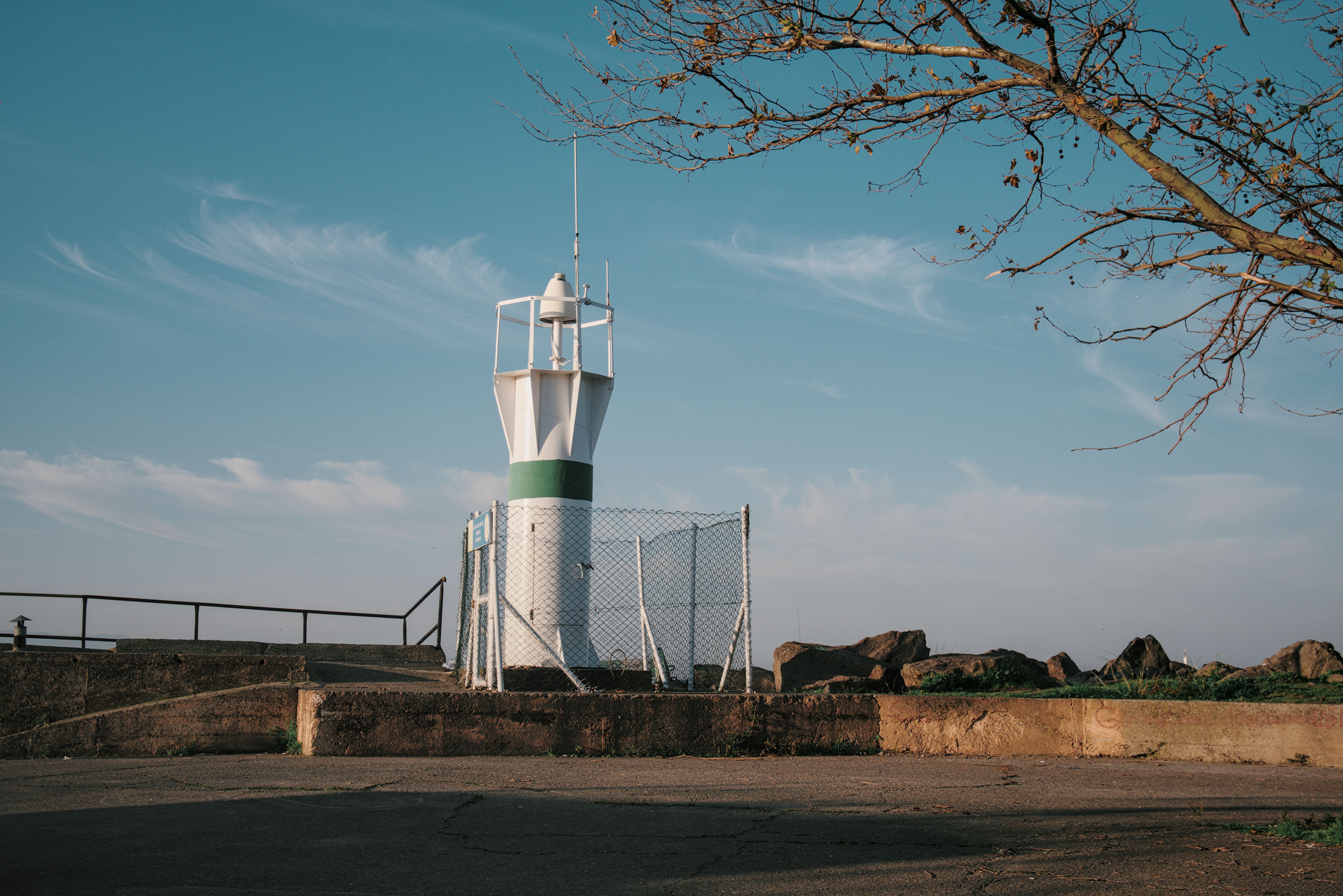 A small lighthouse by the sea on a clear day, surrounded by rocks and bare trees.