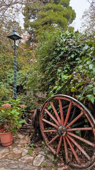 Rustic wagon wheel leaning on foliage with a classic lamppost in a serene garden.