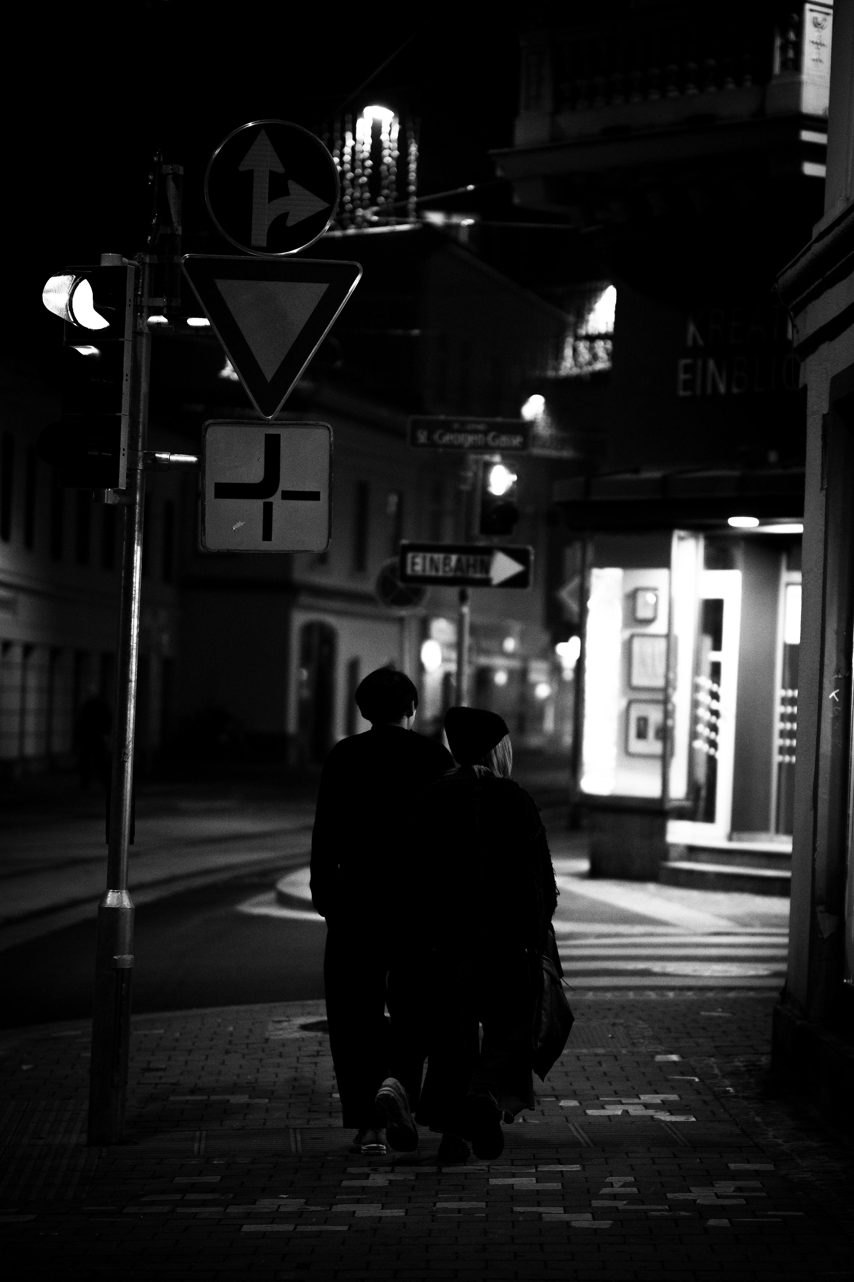 Free A couple walks under streetlights at night in a city, creating a moody urban scene. Stock Photo
