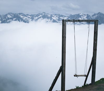 A solitary swing overlooks a mist-covered valley with snow-capped mountains in Rize, Türkiye.