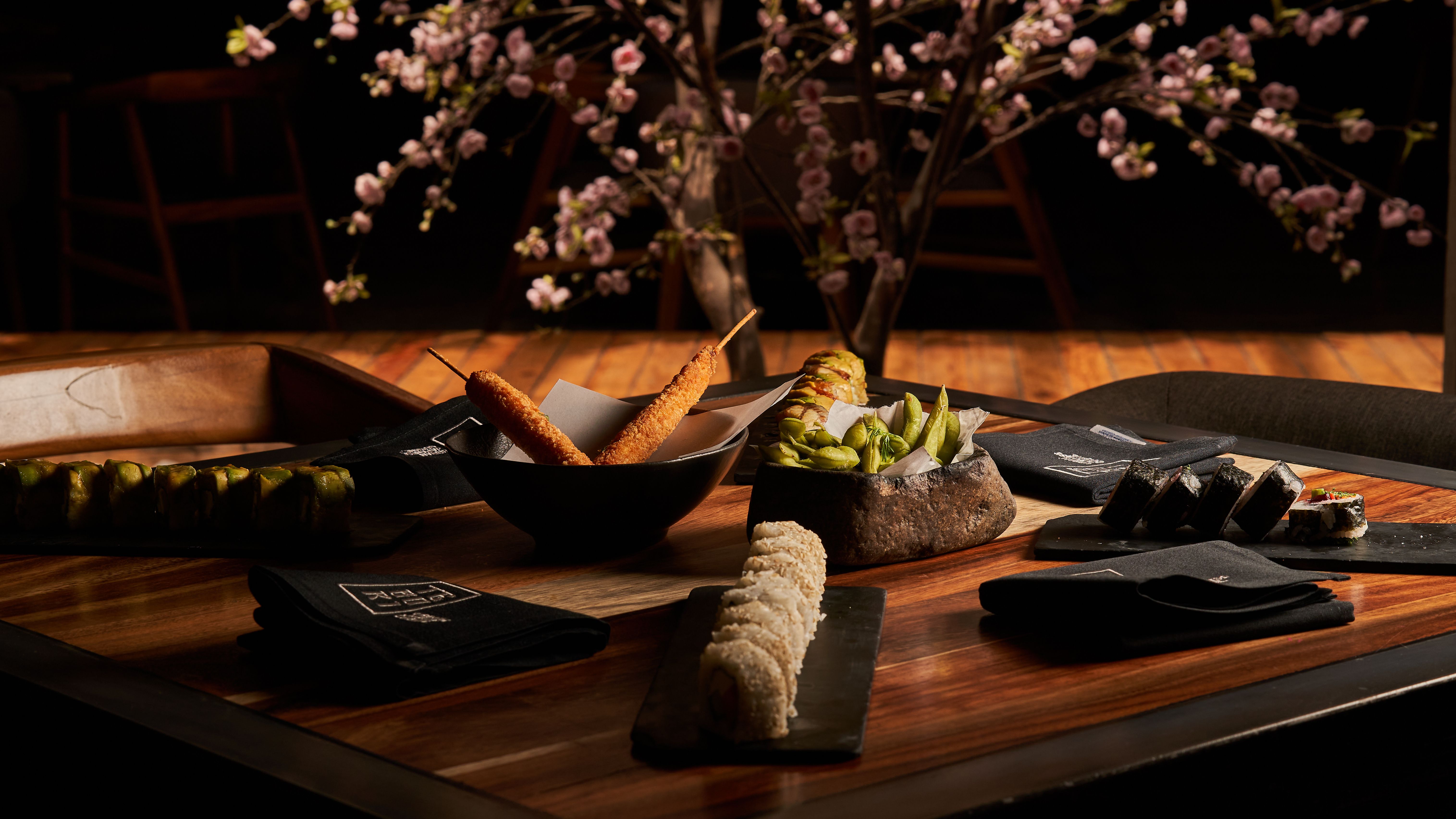 Sushi platter on a wooden table with flowers in the background, lit by warm ambient light