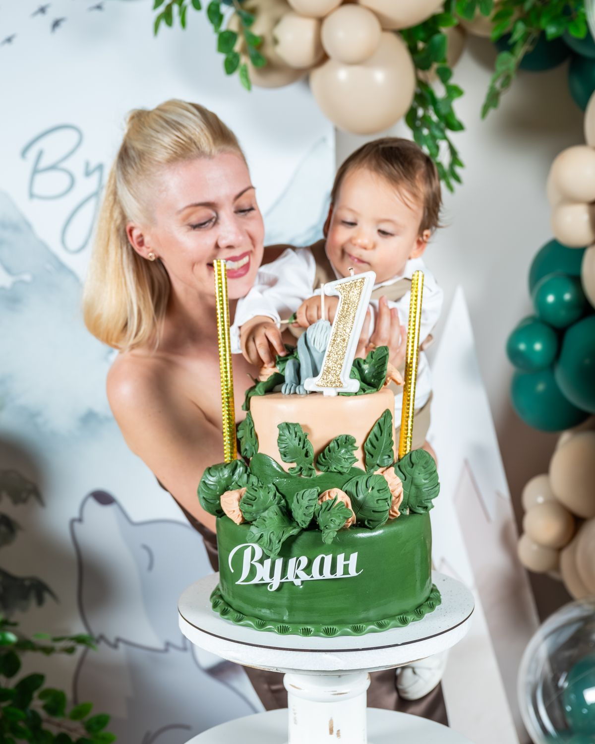 A mother and baby celebrate a first birthday with a beautifully decorated cake indoors. Stock Photo.