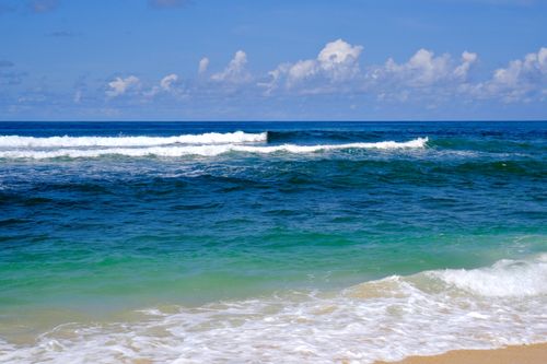 Free Bright blue ocean waves gently crashing on a sandy shore under a clear sky. Stock Photo