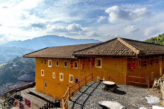 Scenic view of a traditional Fujian Tulou with mountains in the background under clear skies.