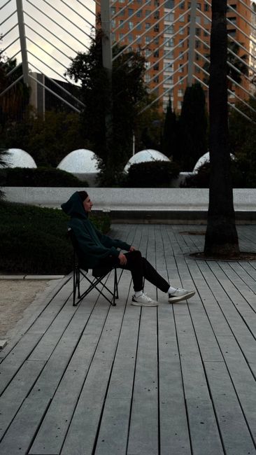 Fotomural Joven adulto en sudadera sentado en un parque de la ciudad con arquitectura moderna.