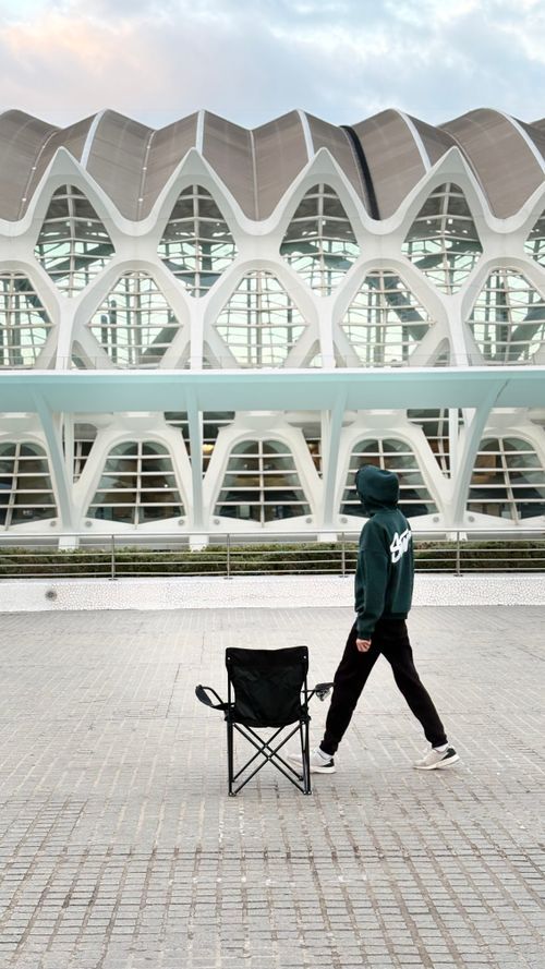 Free A person walks past a modern architectural building with an empty chair in front. Stock Photo