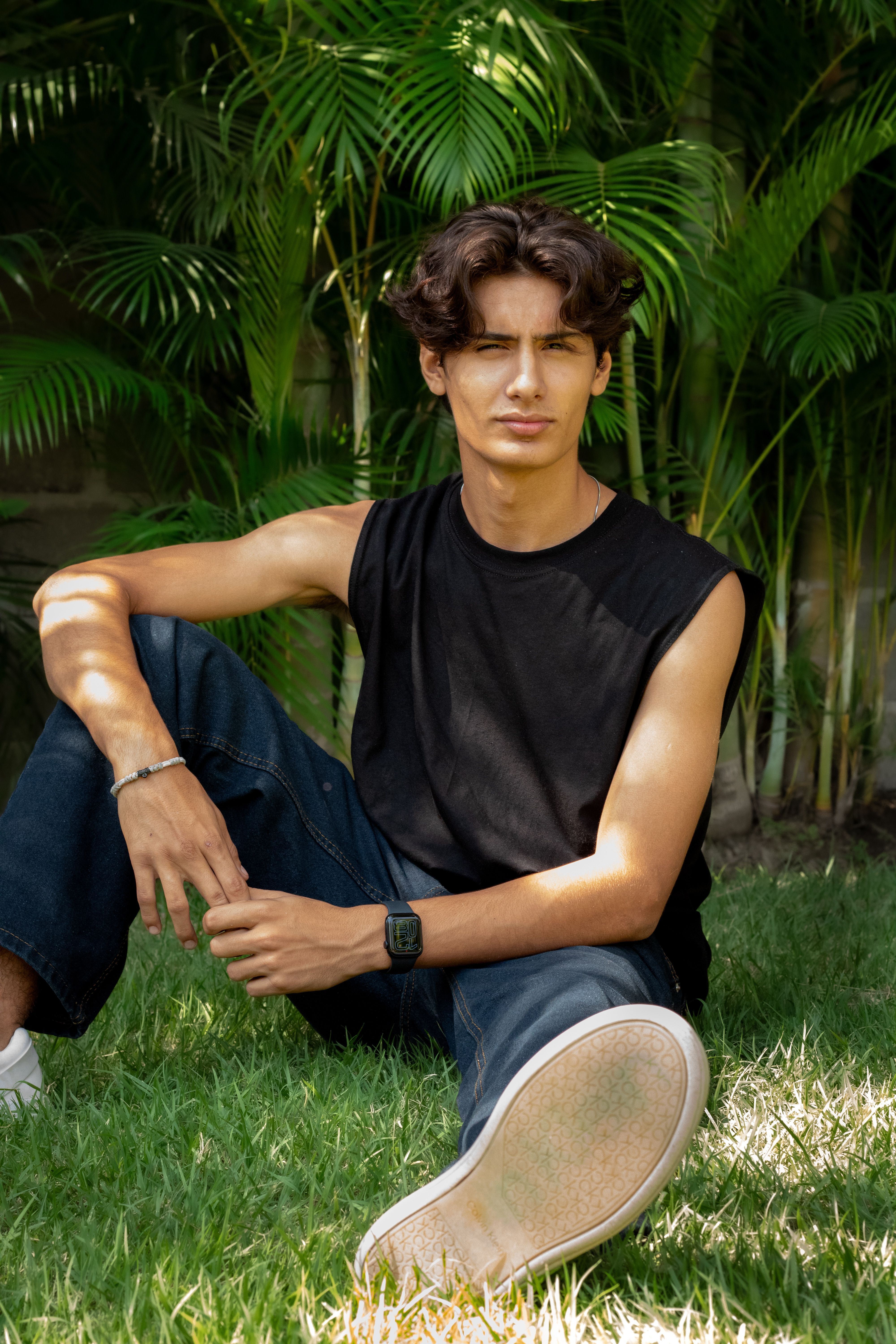 A relaxed young adult sitting on grass, enjoying the sunny day outdoors. Perfect for lifestyle and fashion content.