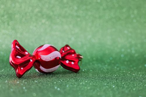 Free Close-up of a shiny red candy ornament on a glittering green background, evoking festive charm. Stock Photo