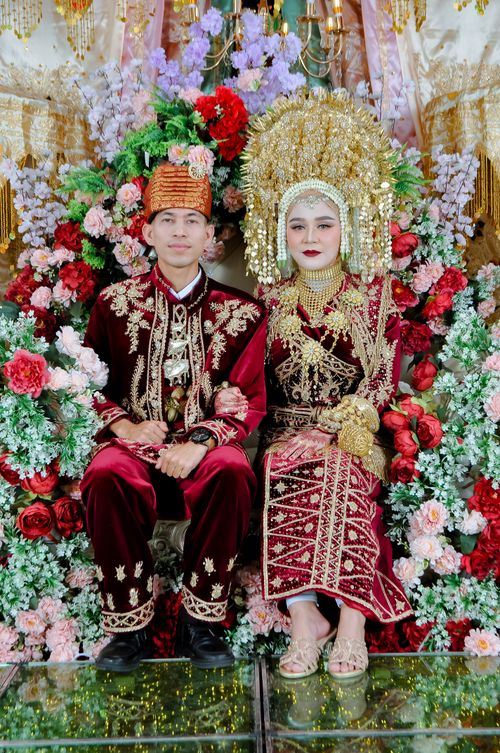 Free Couple in vibrant traditional wedding costumes sitting amidst ornate floral decorations. Stock Photo