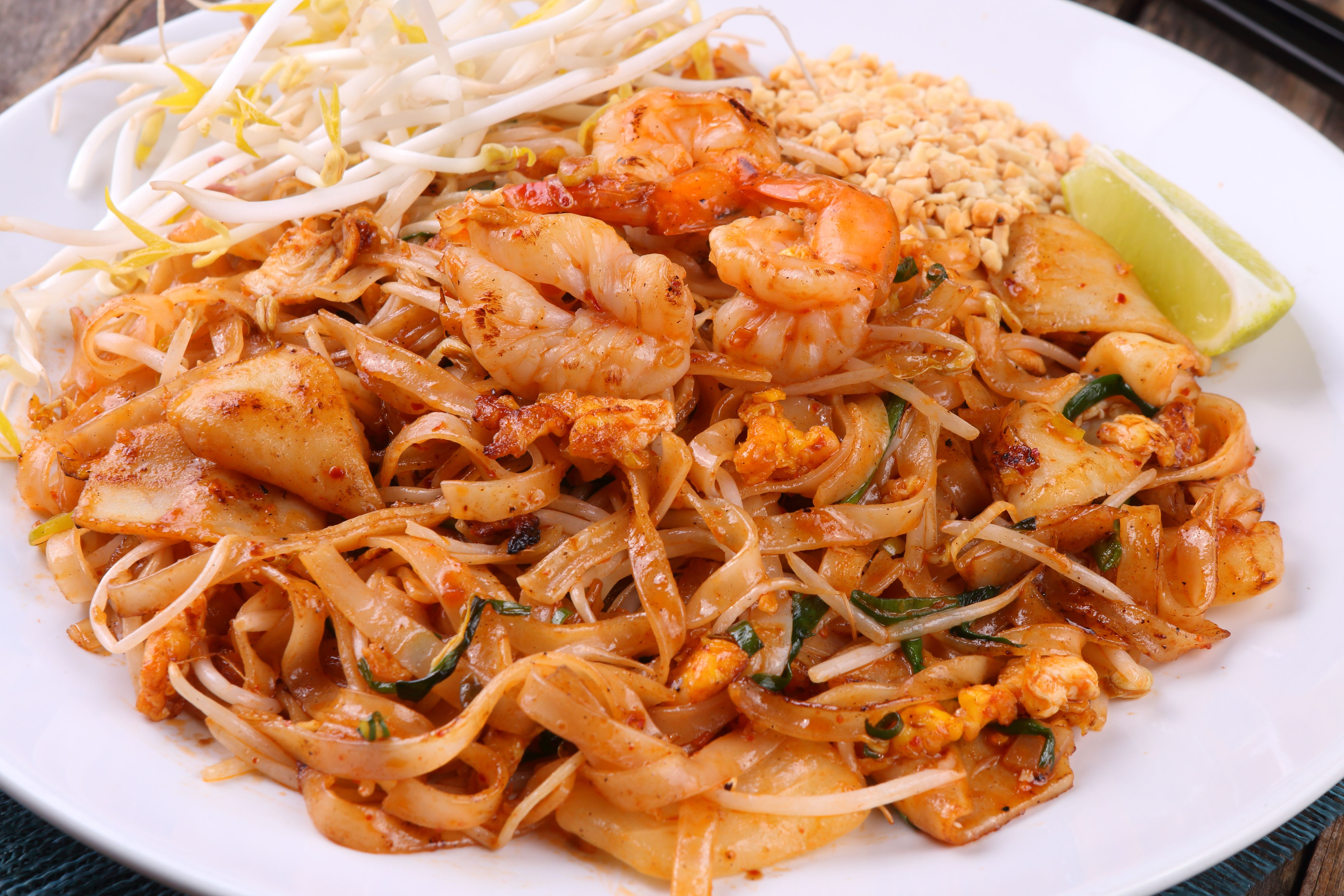 Colorful plate of Thai shrimp pad Thai with lime, peanuts, and bean sprouts.