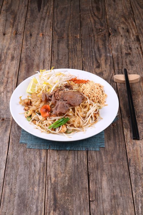Free Delicious Pad Thai with beef, vegetables, and peanuts served on a rustic wooden table. Stock Photo