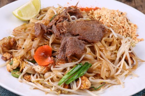 Free Close-up of Pad Thai with beef, vegetables, peanuts, and lime slice on a white plate. Stock Photo
