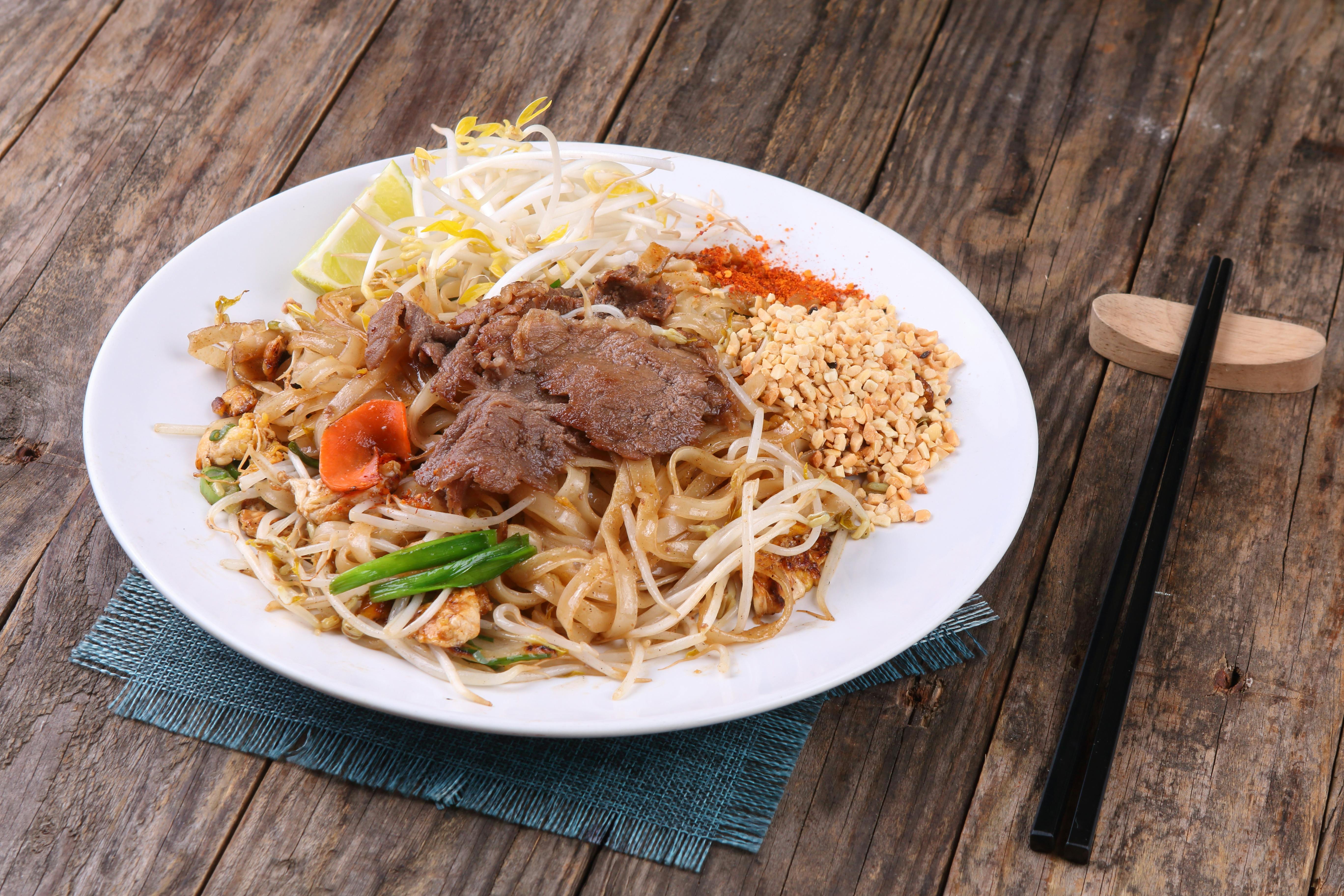 A vibrant plate of Pad Thai noodles garnished with beef, peanuts, and vegetables on a rustic wooden table.